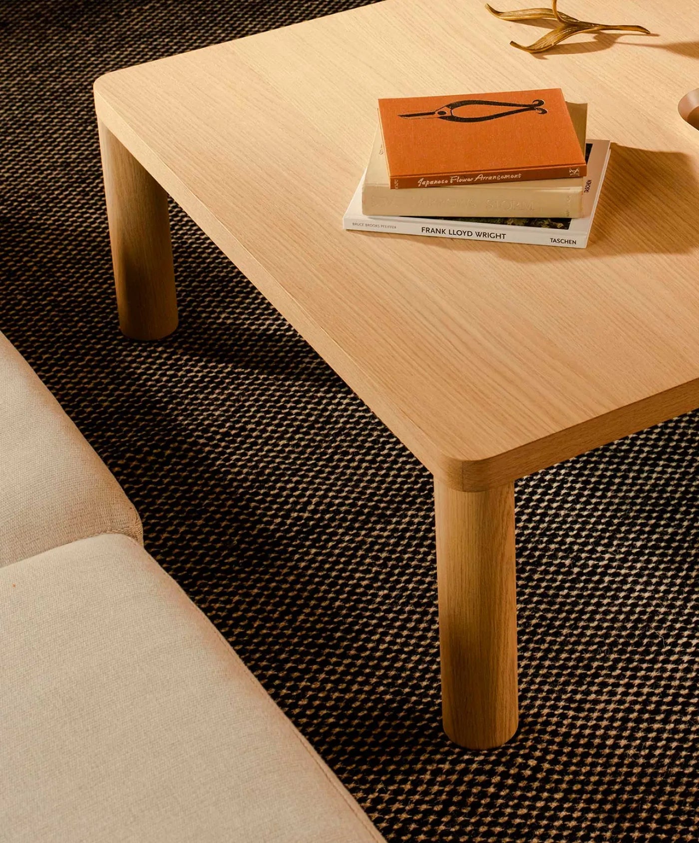 Wooden coffee table with stacked books on a patterned rug next to a beige couch.