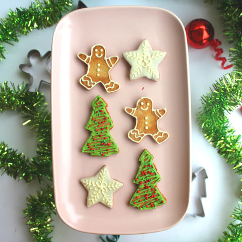 Gingerbread cookies in the shape of a gingerbread man, a christmas tree and a star are placed on a tray next to their cookie cutters