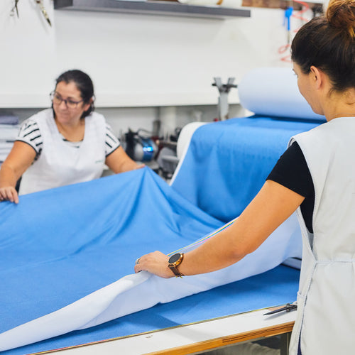 Taller de confección con trabajadoras estirando rollos de tejido Sepiia