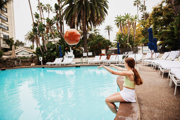 girl sitting on the edge of a pool throwing a beach ball - Best Bra for Small Boobs - Non Disclosure Apparel