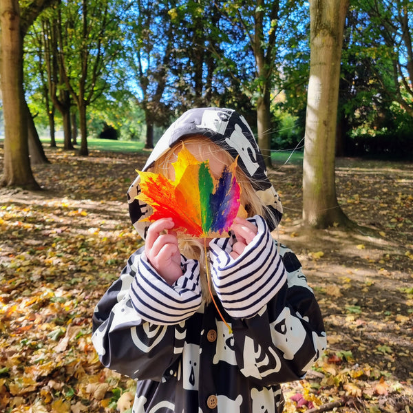 child holding autumn leaf painted rainbow colours