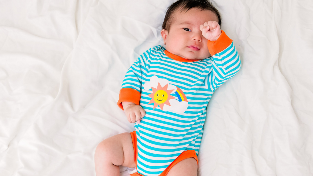 A baby wearing a striped bodysuit with a sun character design from new sustainable baby brand Ducky Zebra