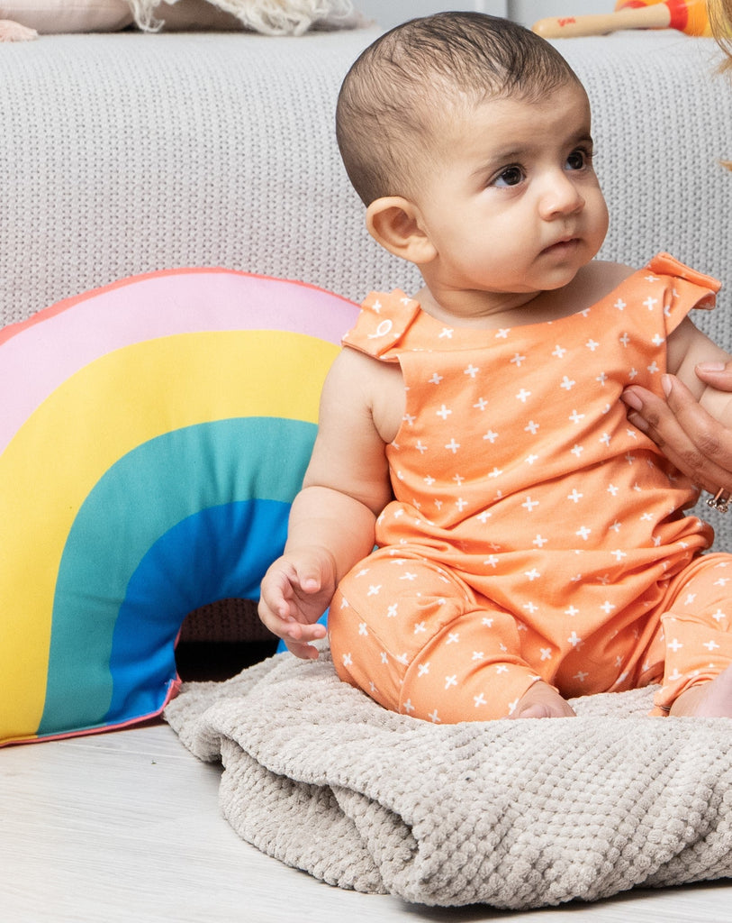 A baby wearing the organic cotton mango crosses baby romper with a rainbow cushion in the background