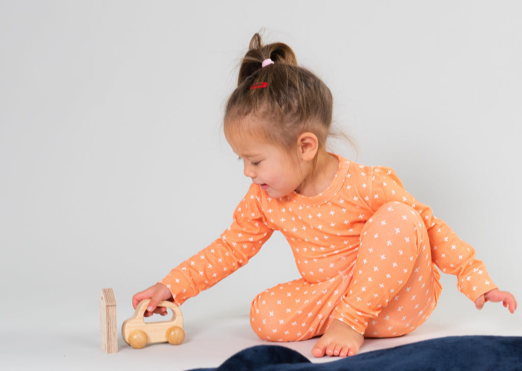 A little girl wearing Roc + Rudi mango crosses pyjamas playing with a wooden toy
