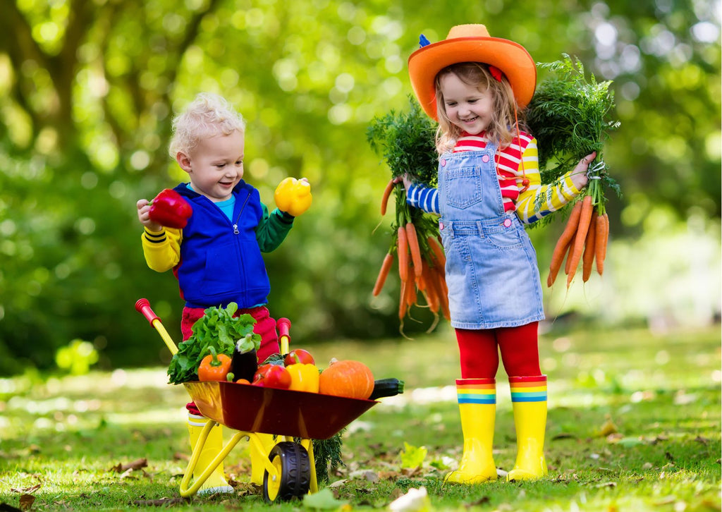 Small children dressed up as farmers with a wheelbarrow of vegetables
