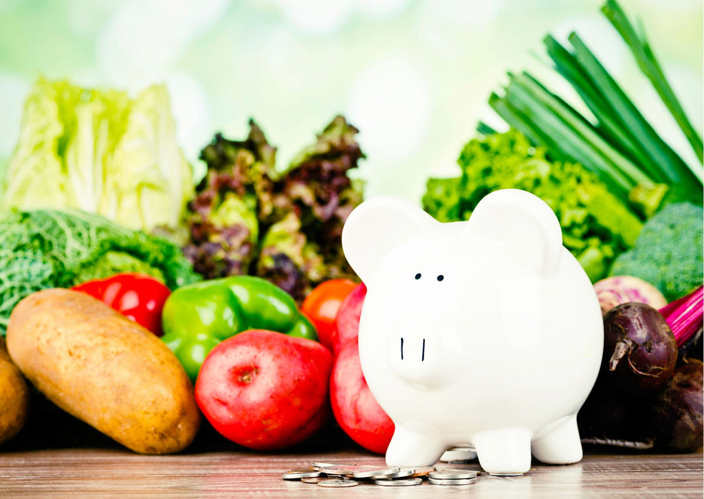 A piggy bank and coins in front of assortment of vegetables