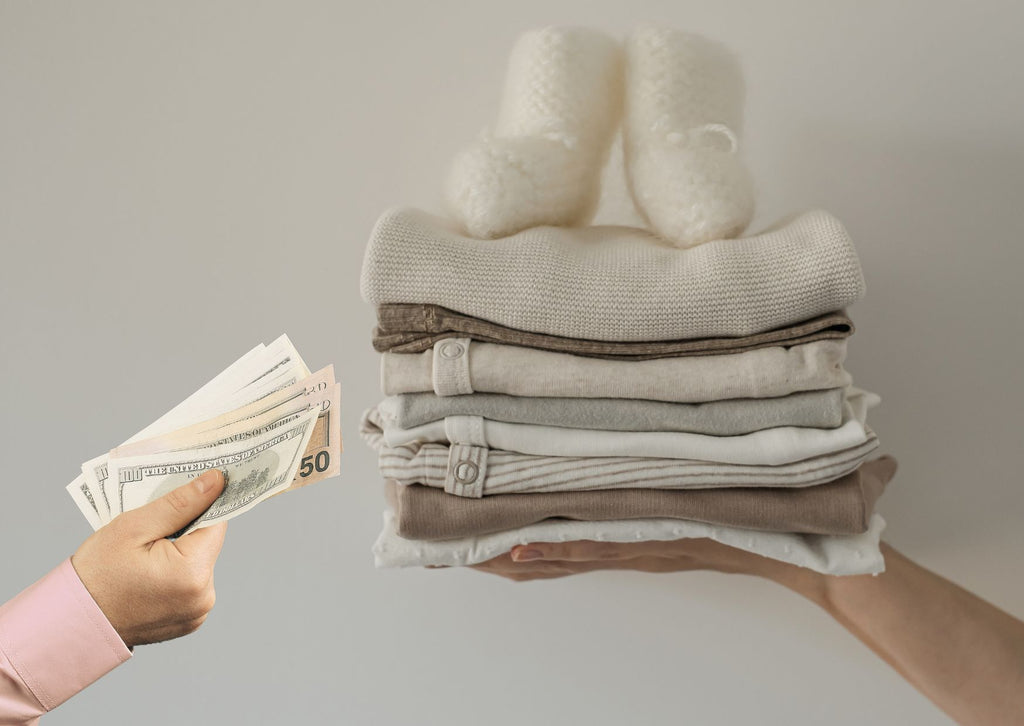 A hand offering cash for a stack of baby clothes