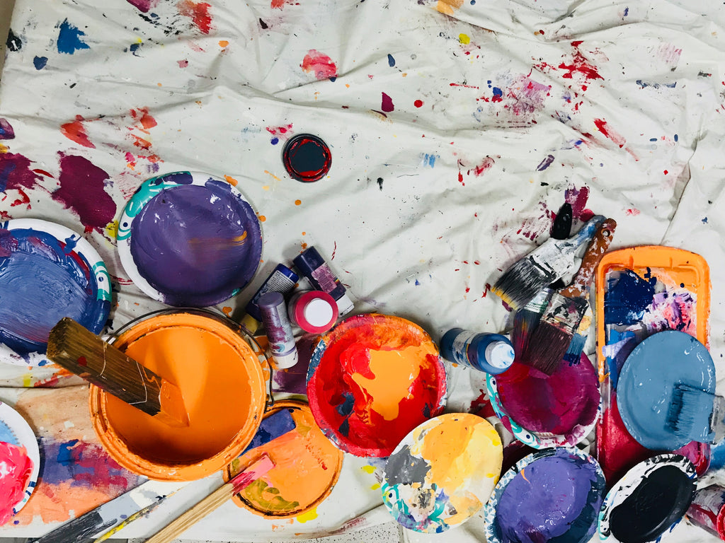 messy floor, paint cans, paintbrushes, orange, purple, pink