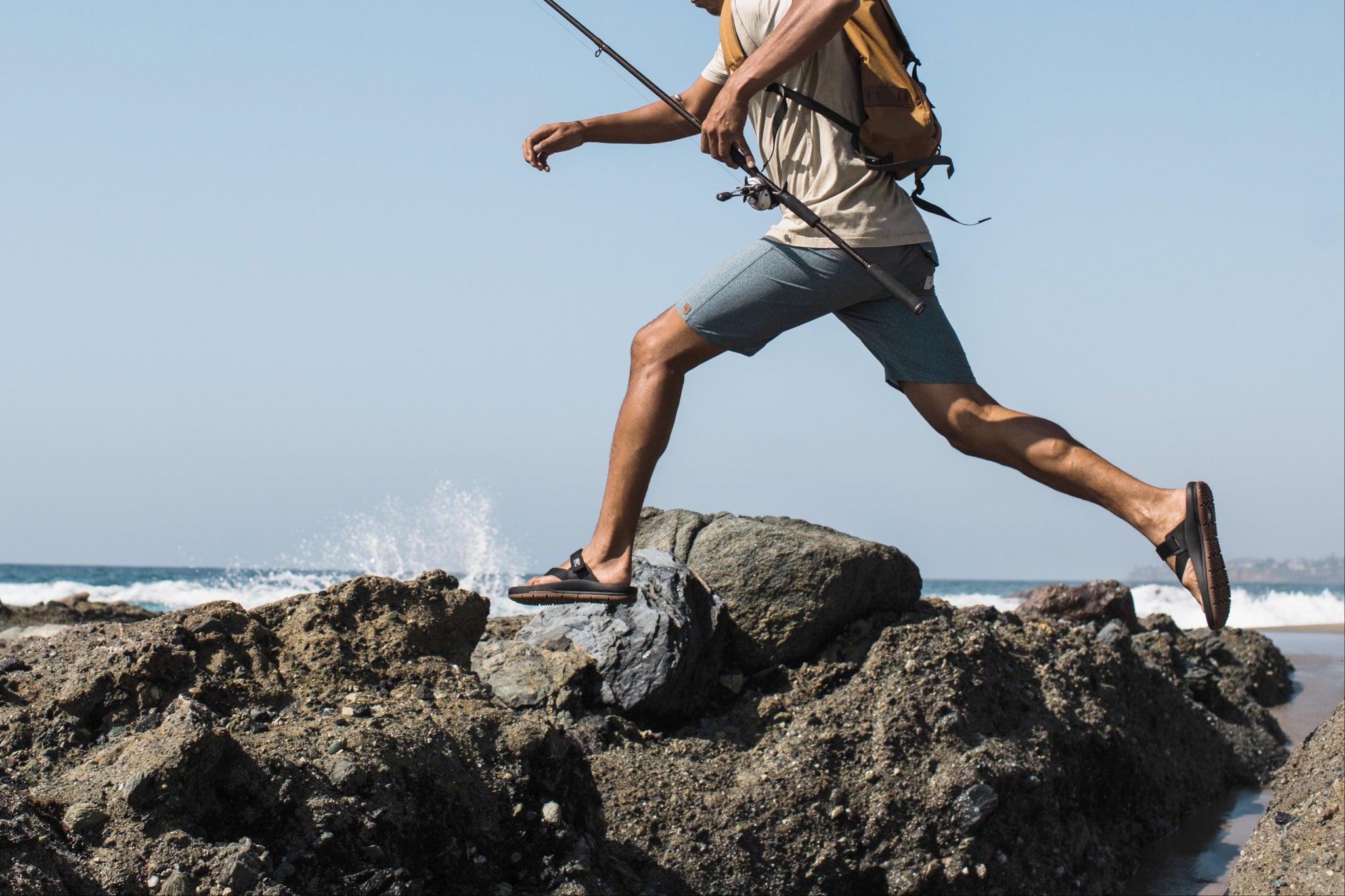 Man in sandal jumping across rocks on beach