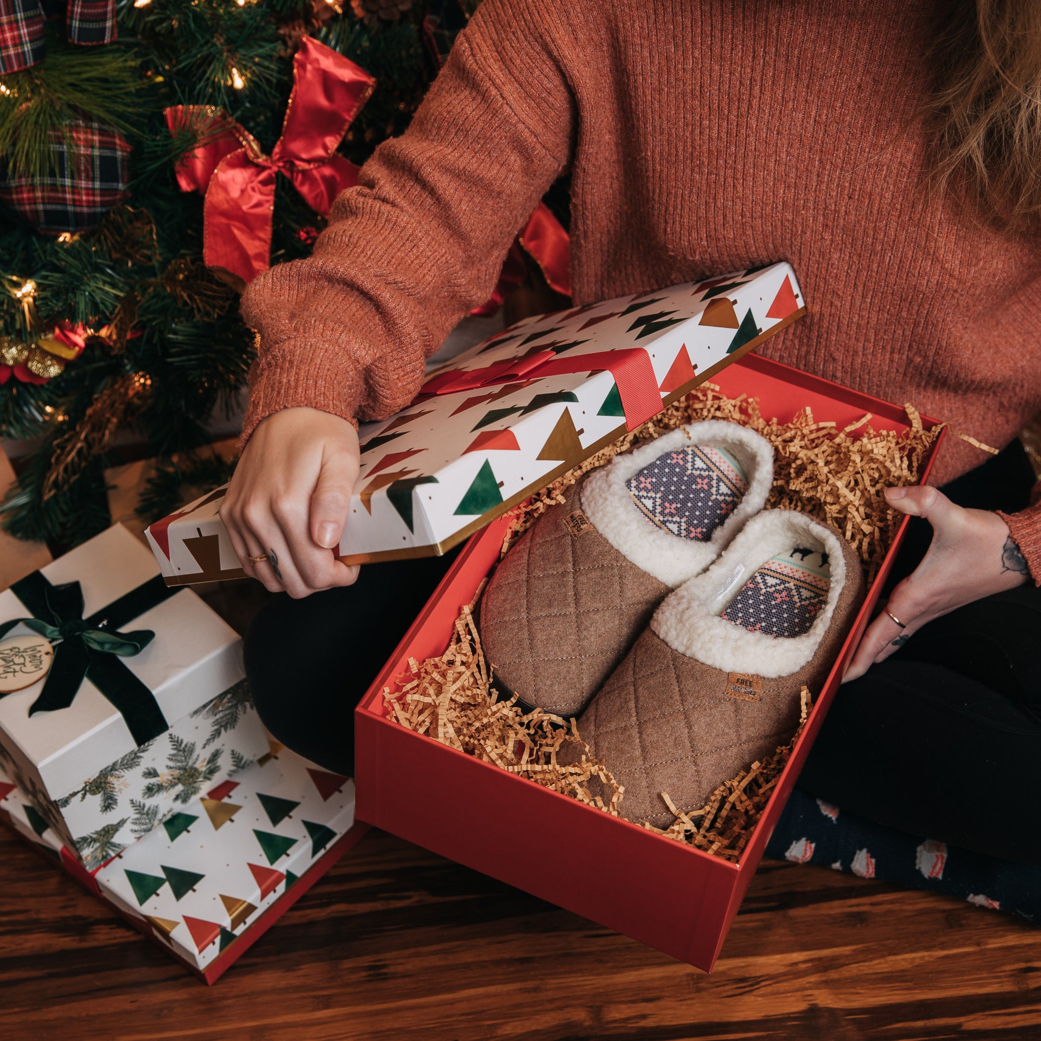 Women opening a gift with slippers inside box by a holiday tree