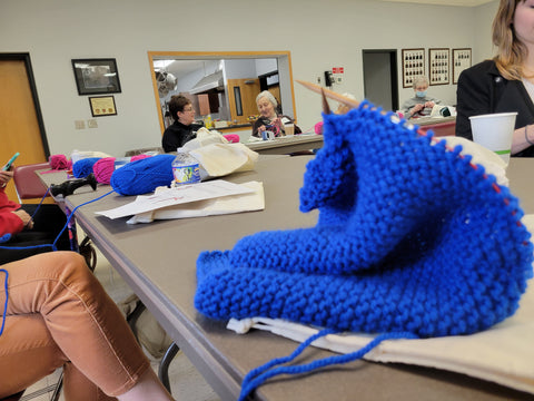 Blue knit blanket in the process of being knit with knitters in the background