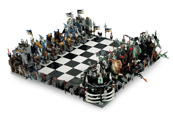This image shows the LEGO Giant Castle Chess Set fully assembled and ready for play. The chessboard is a large gray and black checkered surface flanked by diverse medieval-themed LEGO minifigures. Each chess piece is represented by a figure such as knights, skeletons, wizards, and trolls, adding a fantastical element to the traditional game. The set is meticulously organized, with each side poised for a strategic battle, bringing the fantasy of LEGO to the classic game of chess.