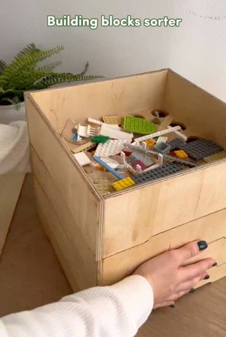 a gif of lego bricks being sorted through a wooden box device