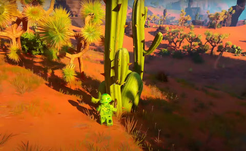 A Lego character in a green suit interacting with a large green cactus in a vibrant, sunlit desert environment with scattered trees and mountains in the distance.