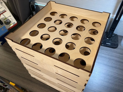 An empty wooden storage box with multiple layers, each featuring circular cutouts designed to organize small items, on a desk.
