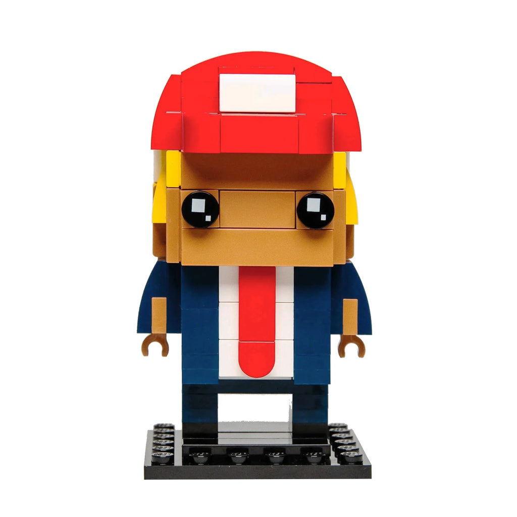 Custom Lego BrickHeadz caricature of President Trump with distinctive hairstyle in blue suit and red tie, against a white background.