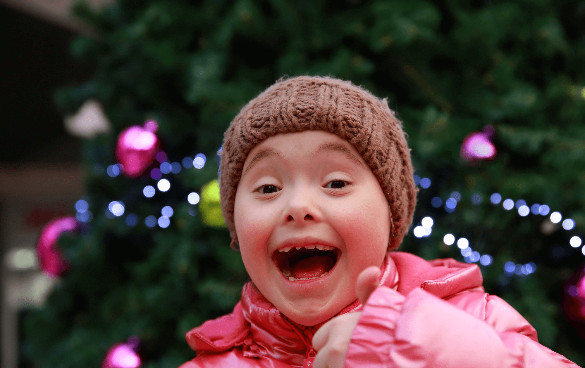 child smiling in front of christmas tree ready to give gifts