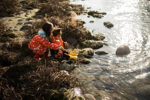 Due bambine giocano in riva al fiume indossano giacche impermeabili colorate
