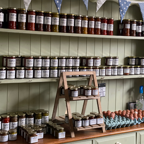 Glass jars of jam, preserve and chutneys are displayed on an antique dresser at Oaktrack farm shop. 