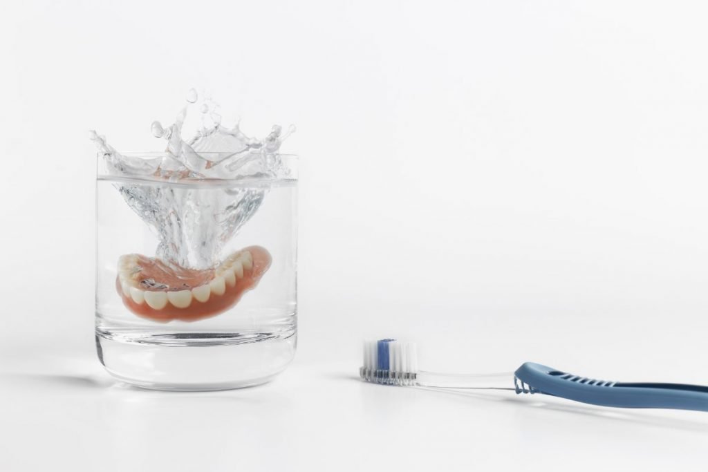 Care tips for dentures. Prosthesis in glass with water.