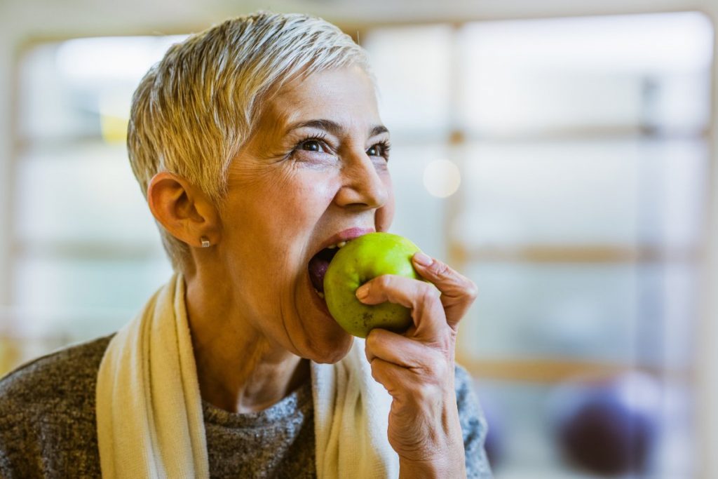 Glimlachende hogere vrouw die in een appel bijt.