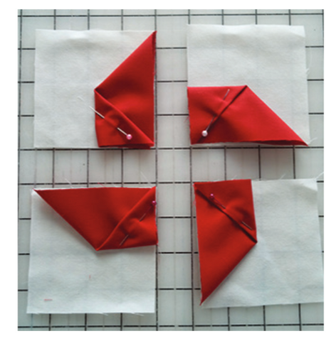 Red fabric shapes pinned onto white fabric squares. Shown on a gridded background.