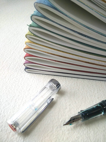Stack of colourful cotton rag notebooks and a fountain pen