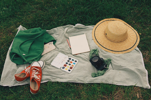 Blanket on grass with hat, camera, notebook, and satchel