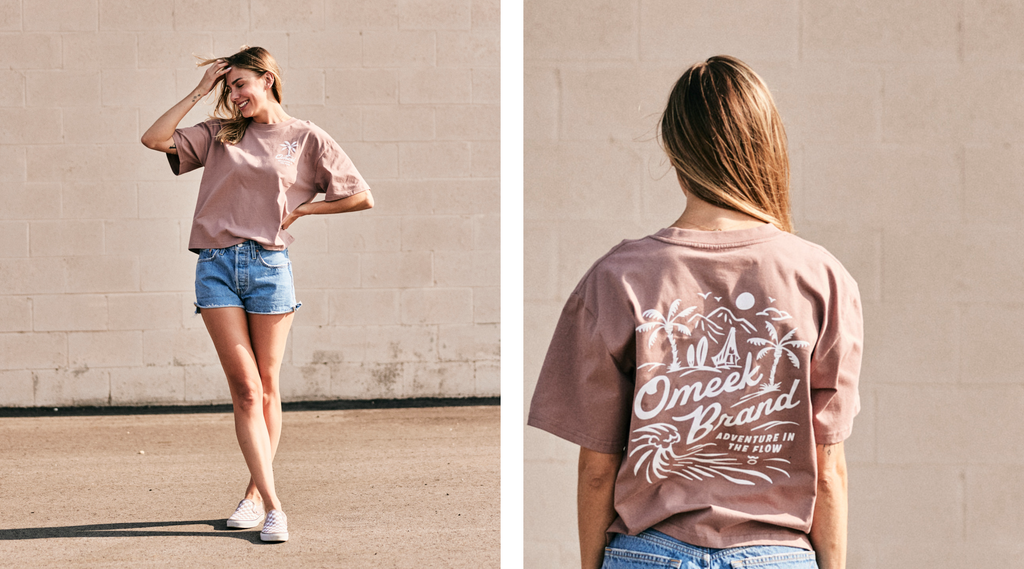 Women modeling a Omeek brand tee shirt with a palm tree and ocean graphic