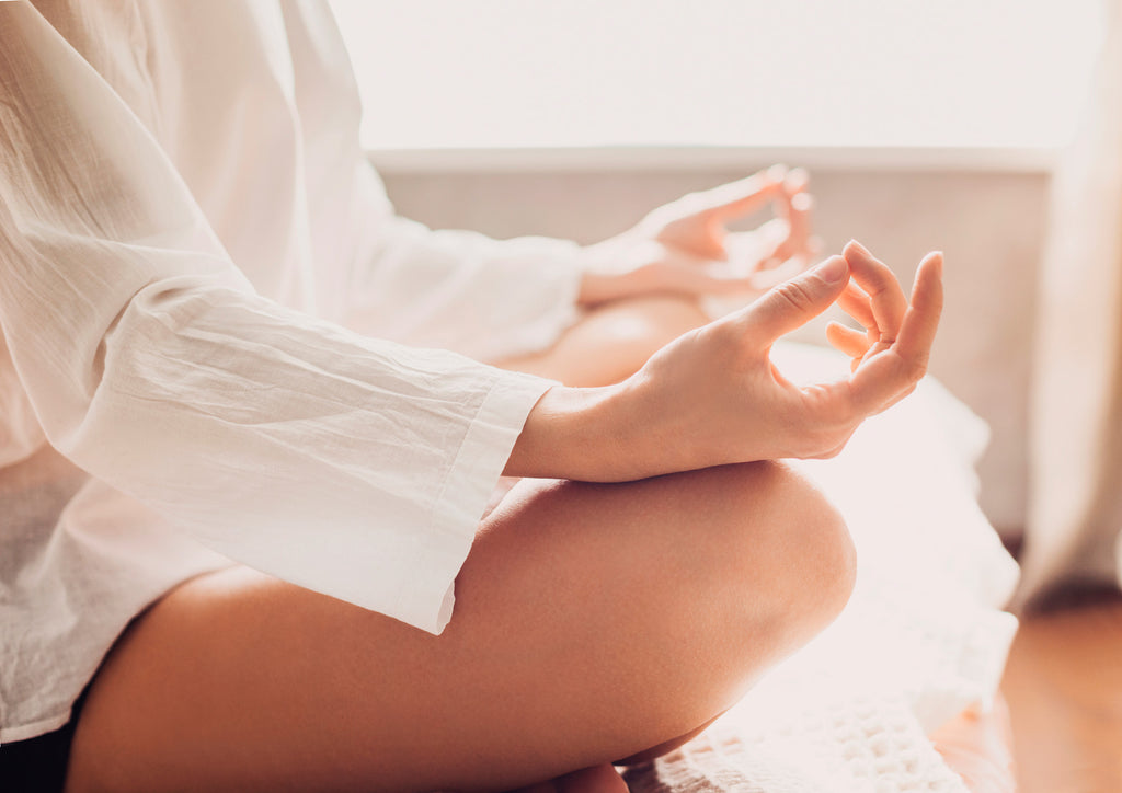 Uma mulher está sentada em posição de meditação praticando momento mindfulness