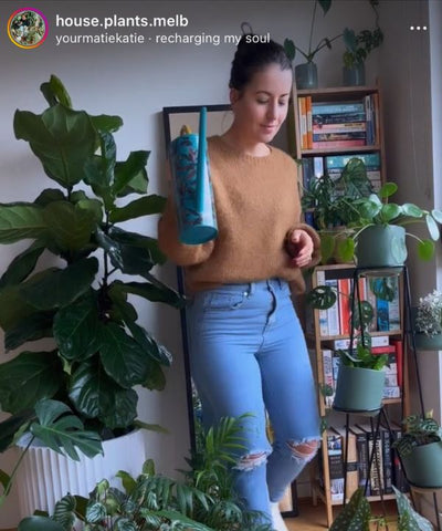@house.plants.melb holds a watering can while she carefully walks among her indoor plants.