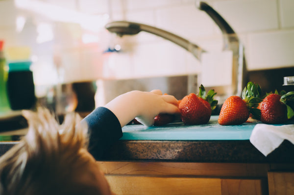 child reaching for strawberries on countertop