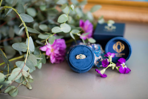 A unique engagement ring in a velvet box surrounded by flowers
