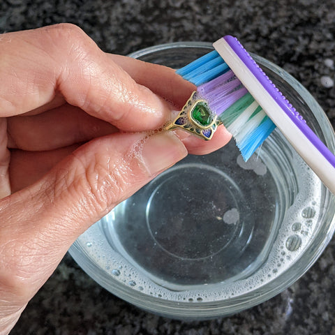 Scrubbing a gold ring gently with a toothbrush and soapy water to remove clean the ring