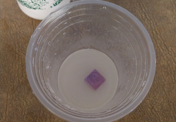 a single purple dice floating in a plastic cup filled with salt water