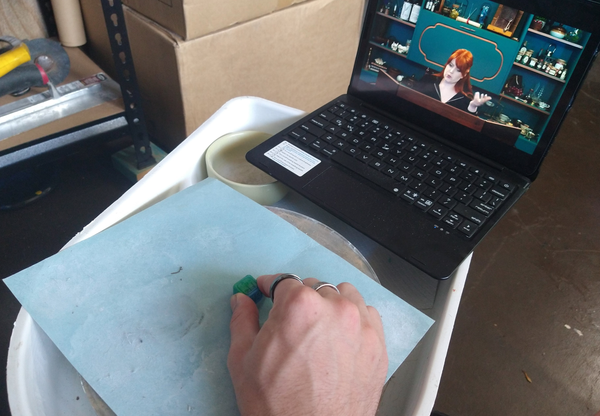 A pottery wheel spinning a polishing paper, and pad, with laptop in the background