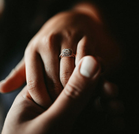 Close up picture of a man's hand holding a woman's hand with an engagement ring