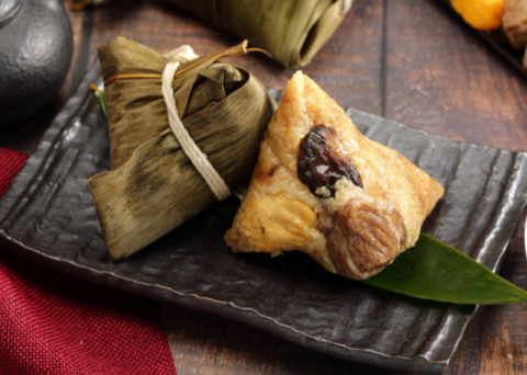 Traditional steamed sticky rice dumplings wrapped up in bamboo leaves served on a black square plate
