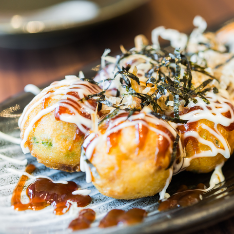 Baked balls of dough stuffed with octopus legs are topped with sauce, mayonnaise and dancing dried bonito flakes