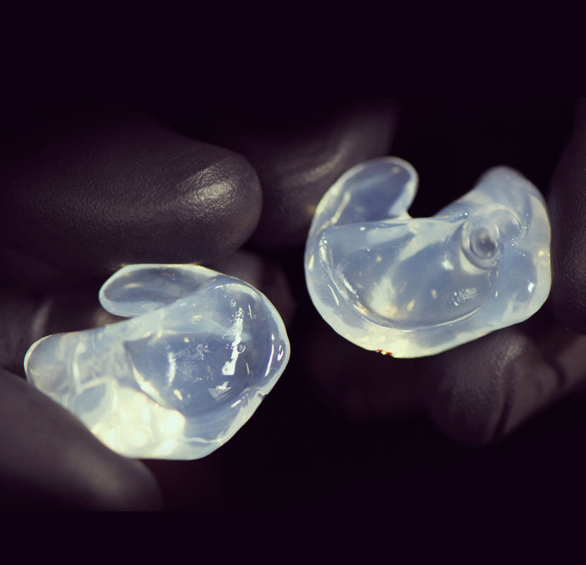 Gloved hand holding a pair of custom silicone eartips in clear color
