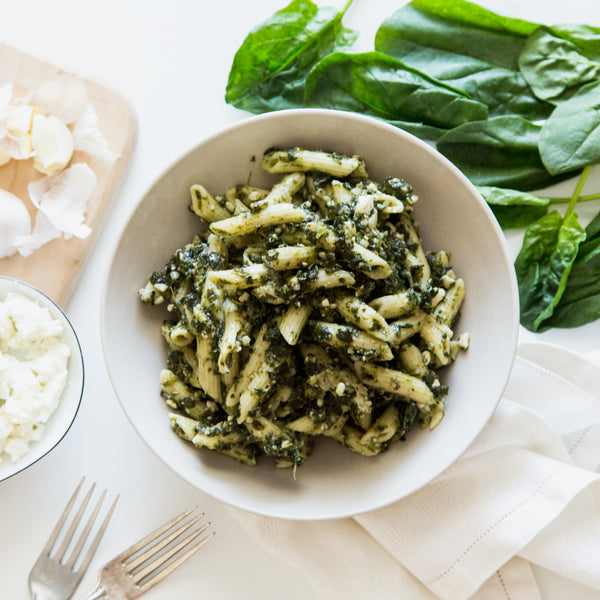 Penne pasta with spinach and feta cheese in a white bowl captured from above with some lettuce around 