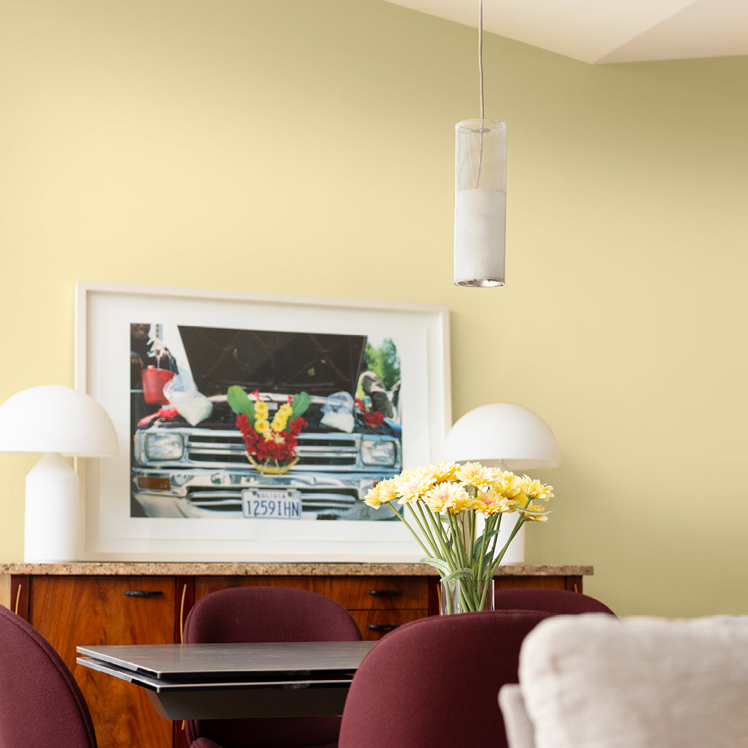 Pale yellow walls painted in Lemon Drizzle Cake by Curator Paints with glass dining table and dark wooden drawers