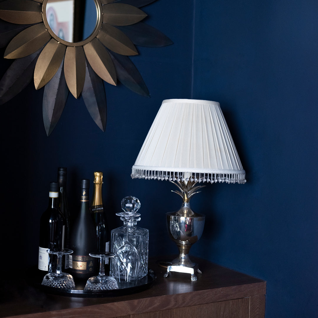 Dark navy painted walls with bronze mirror and white lampshade