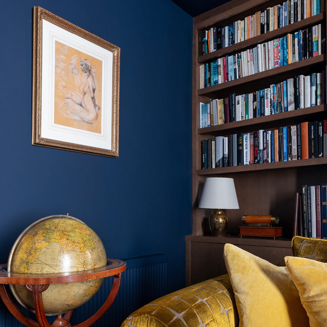 Living room painted in dark navy colour Obscure by Curator Paints. Gold velvet couch, globe and dark wooden bookshelf.