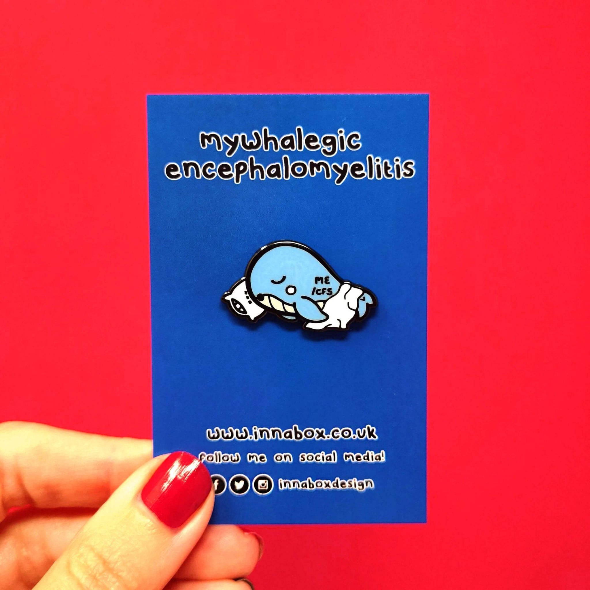 Mywhalegic Enamel Pin - Myalgic Encephalomyelitis (ME/CFS) on blue backing card on a red background. The enamel pin is a sleeping blue whale laying on a white pillow with a white blanket over it and ME/CFS written on its back. The enamel pin is designed to raise awareness for Myalgic encephalomyelitis or chronic fatigue syndrome