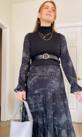 Nicol stands in front of the camera in the black deema sustainable maxi-dress from this is willow. She has pulled a black vest over top, added a belt at her natural waist, chunky gold jewelry and is holding a grey purse