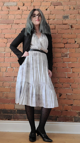 this is willow founder wears the grey ecovero Quinn midi-dress with a black blazer, belt, sheertex and low heels. A brick wall is the background.