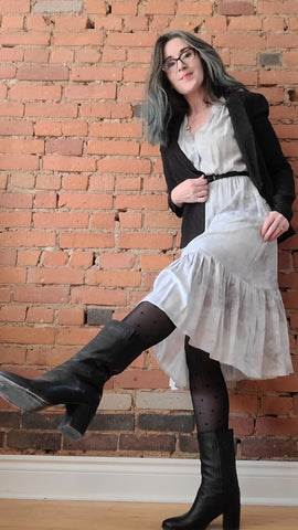 this is willow founder wears the grey ecovero Quinn midi-dress with a black blazer, belt, sheertex and heeled boots. A brick wall is the background.