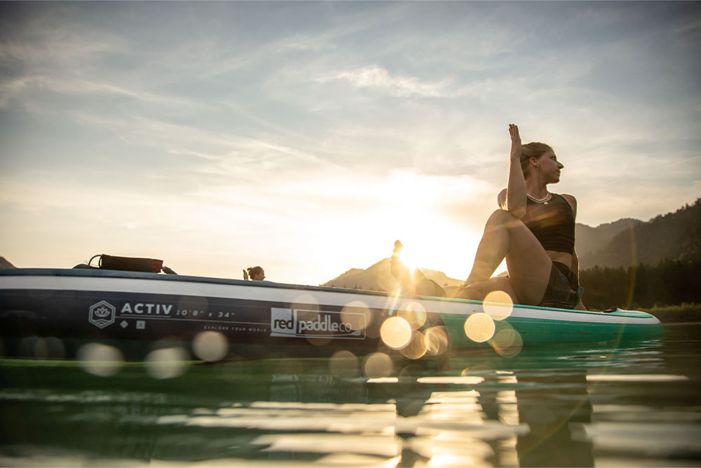 Women Sat On Red Paddle Co Activ 108 Paddle Boards Doing Yoga 