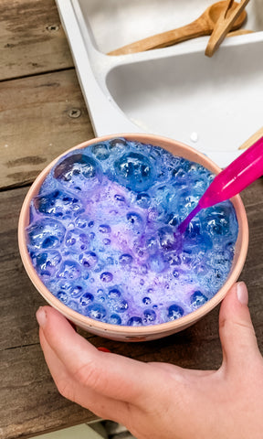 blue, pink, and purple, fizzy potion play in a mud kitchen, wooden outdoor play kitchen, creating fizz with a chemical reactions with water, baking soda, and citric acid.